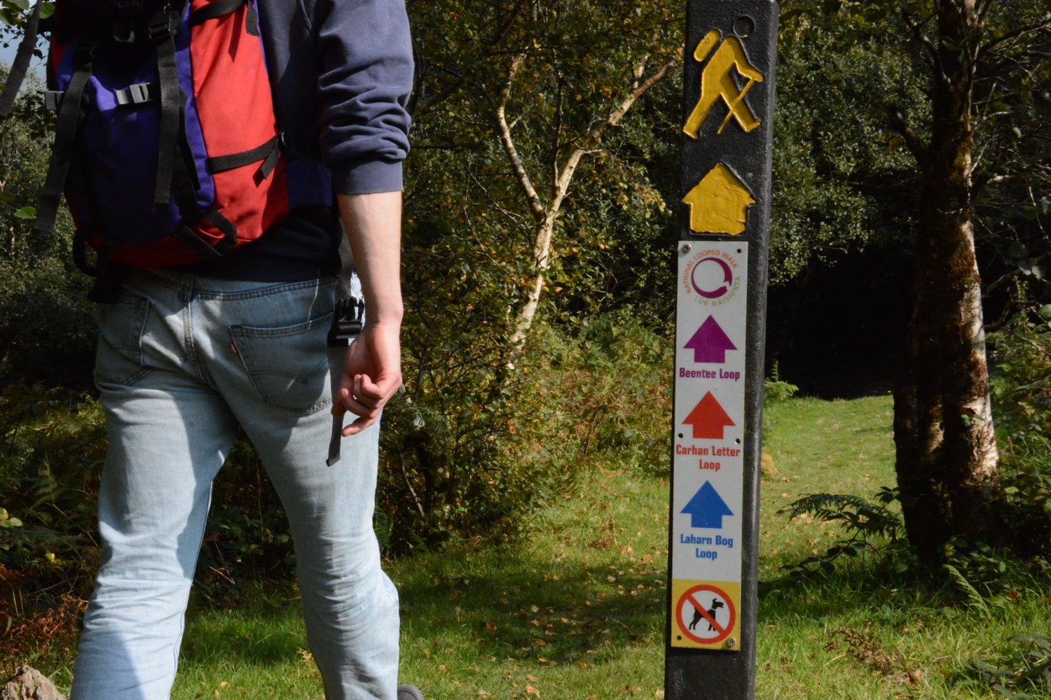 A person with a backpack walking on a path with a trail marker sign