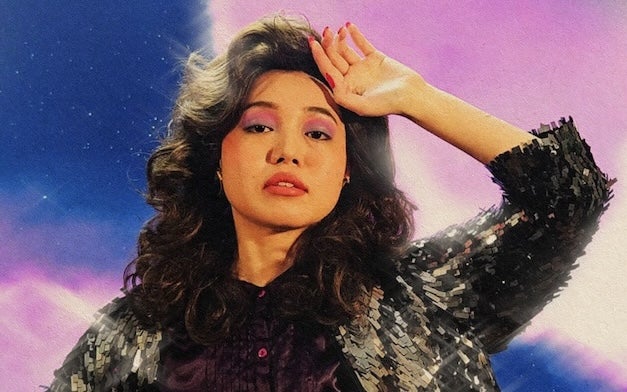 A woman is holding up the back of her hand to her forehead in a slightly dramatic manner.