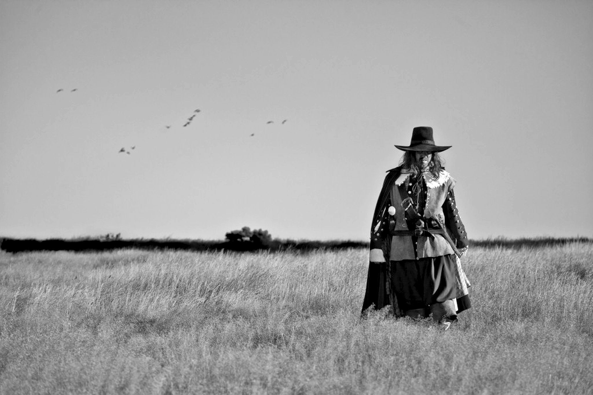 A man dressed in clothes of 17th Century England is walking across a field.