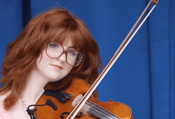 A serious looking young woman holding a violin and bow ready to play