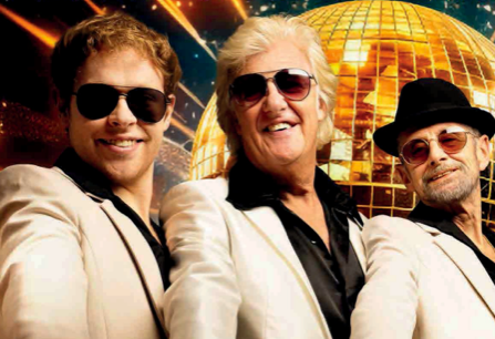 3 smiling men in white suits with dark shirts, all wearing sunglasses with golden, mosaic disco ball in background.