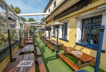 Two rows of wooden picnic benches along the exterior wall of a pub