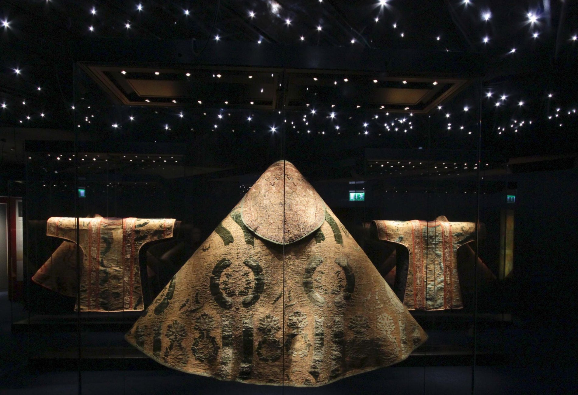 Large gold vestment on display in a dark room with lots of small twinkling lights above it