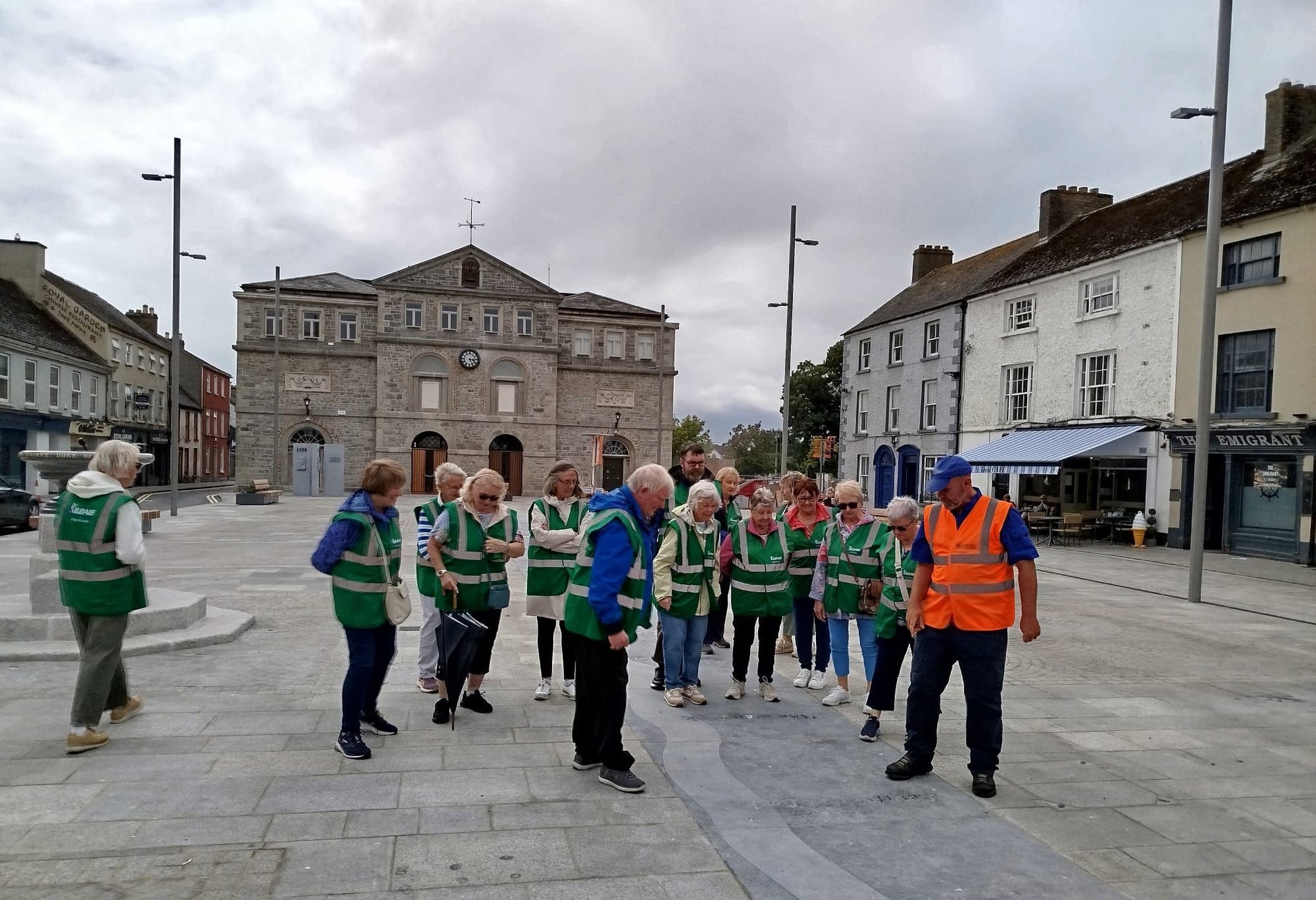 Group wearing green jackets led by a guide in an orange jacket all looking at the ground in Athy