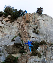 Person climbing while another person holds a rope on top of a rock