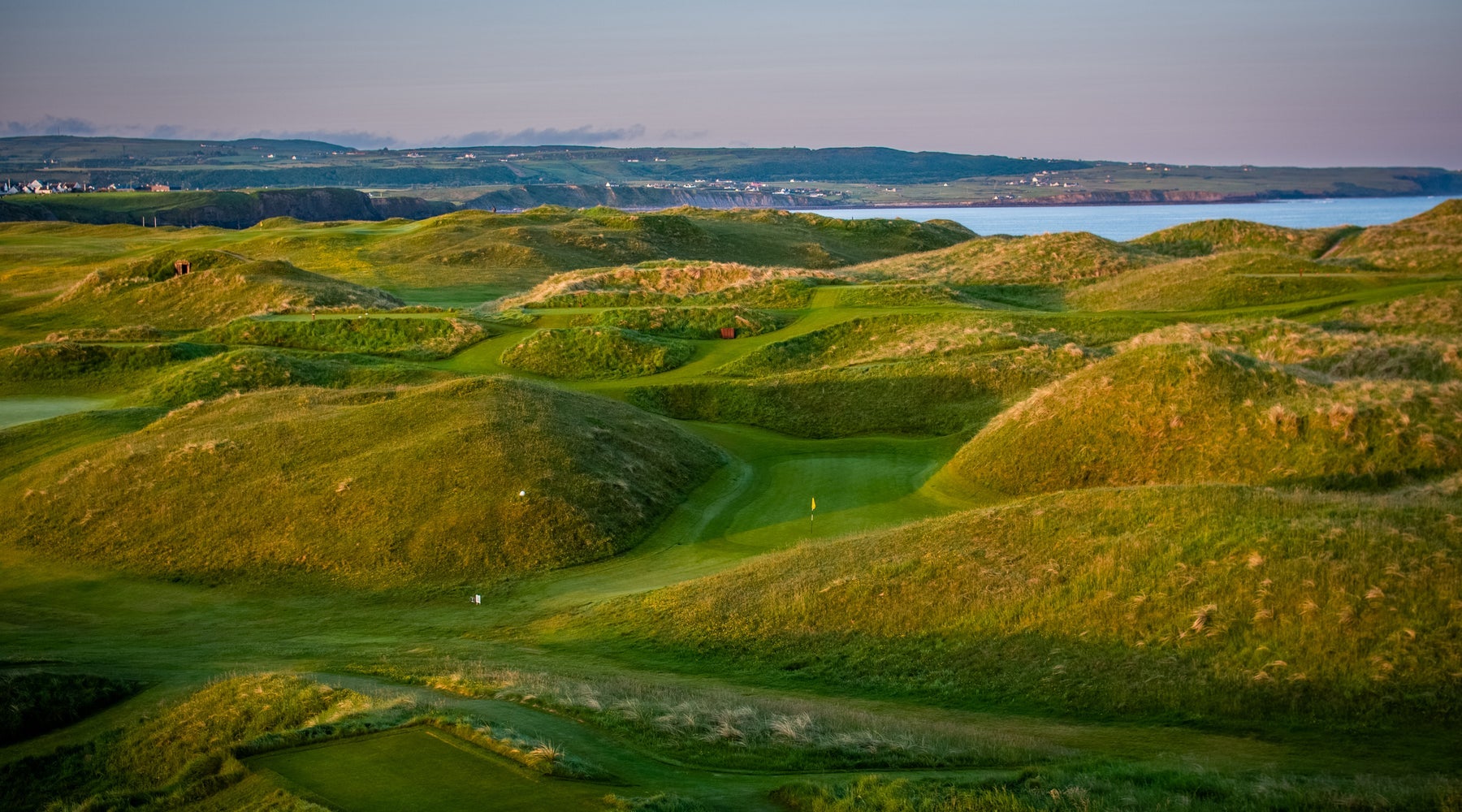 A golf course with grassy dunes and the coast in the distance
