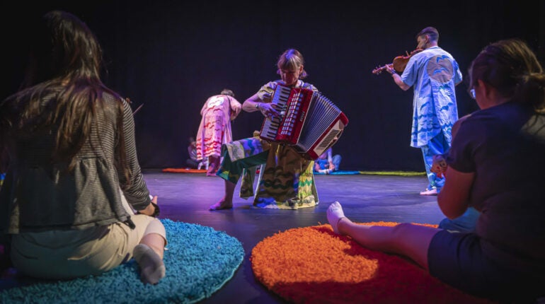Musicians moving around a stage whilst playing to a seated adult and baby