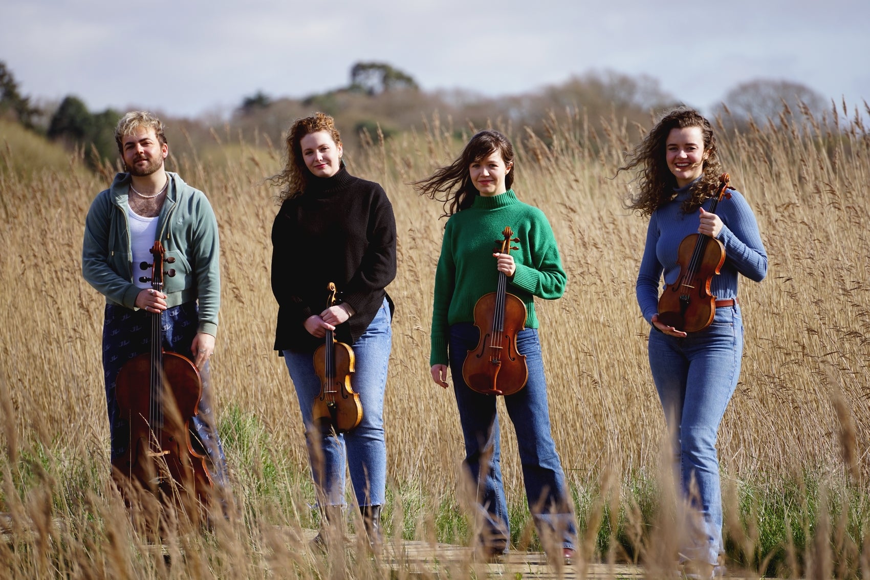 The members of the Calathea Quartet holding their instruments. They're standing on a path surrounded by tall grass.