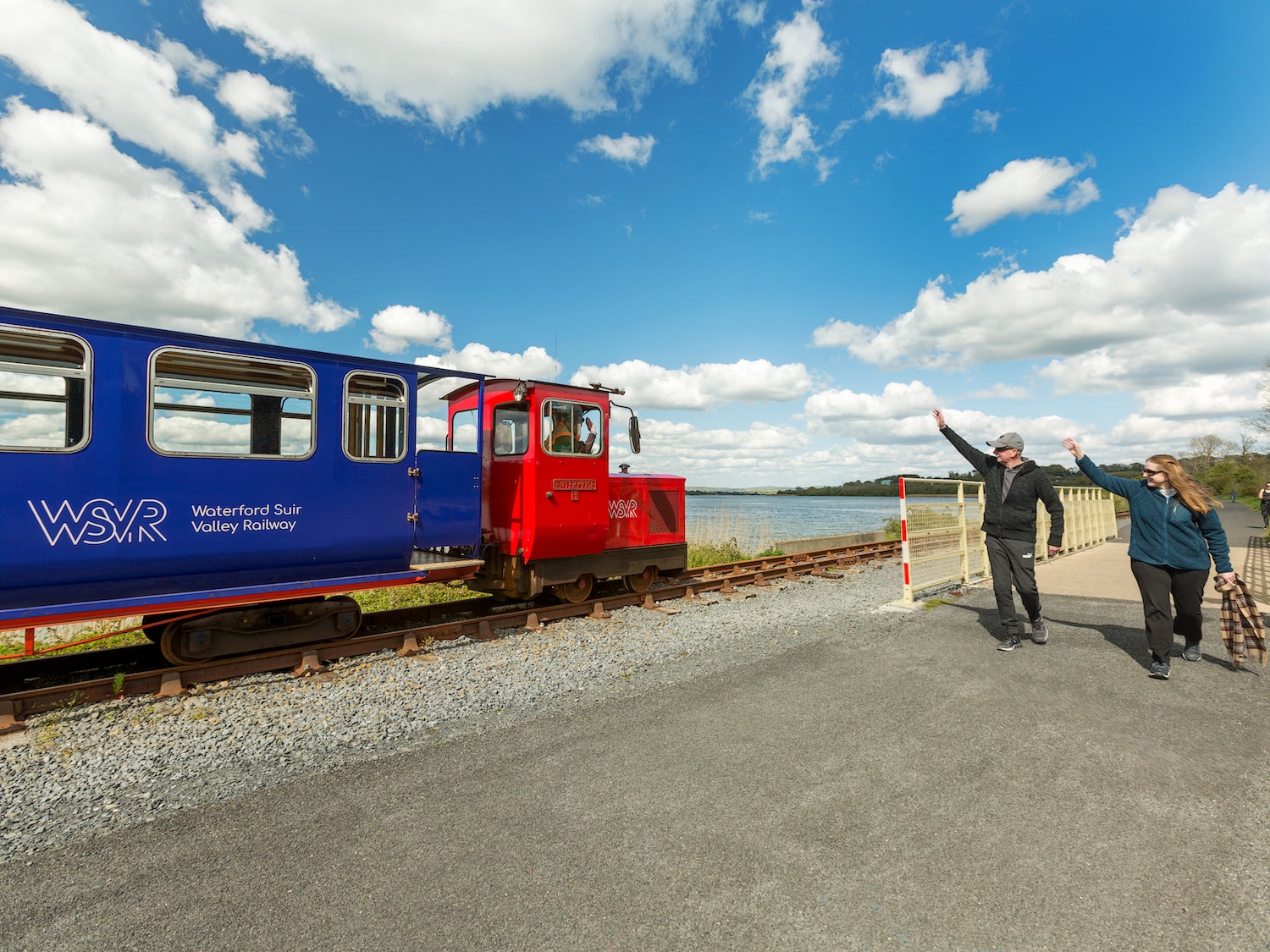 Two people waving at the Waterford Suir Valley Railway train as it goes by in County Waterford.