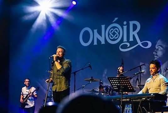 4 men playing and singing on stage.