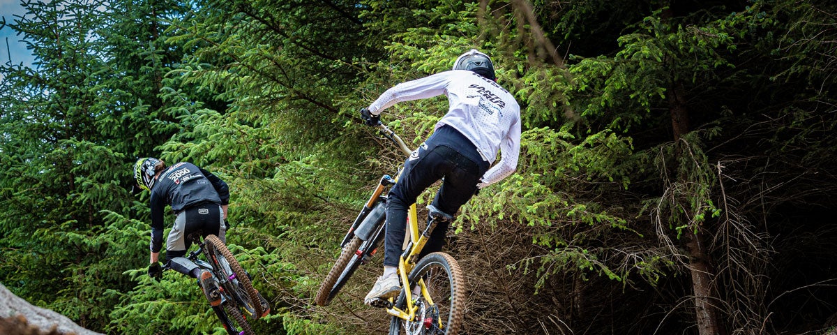 Two bikers mid jump on a forest track beside trees at Glencullen Adventure Park