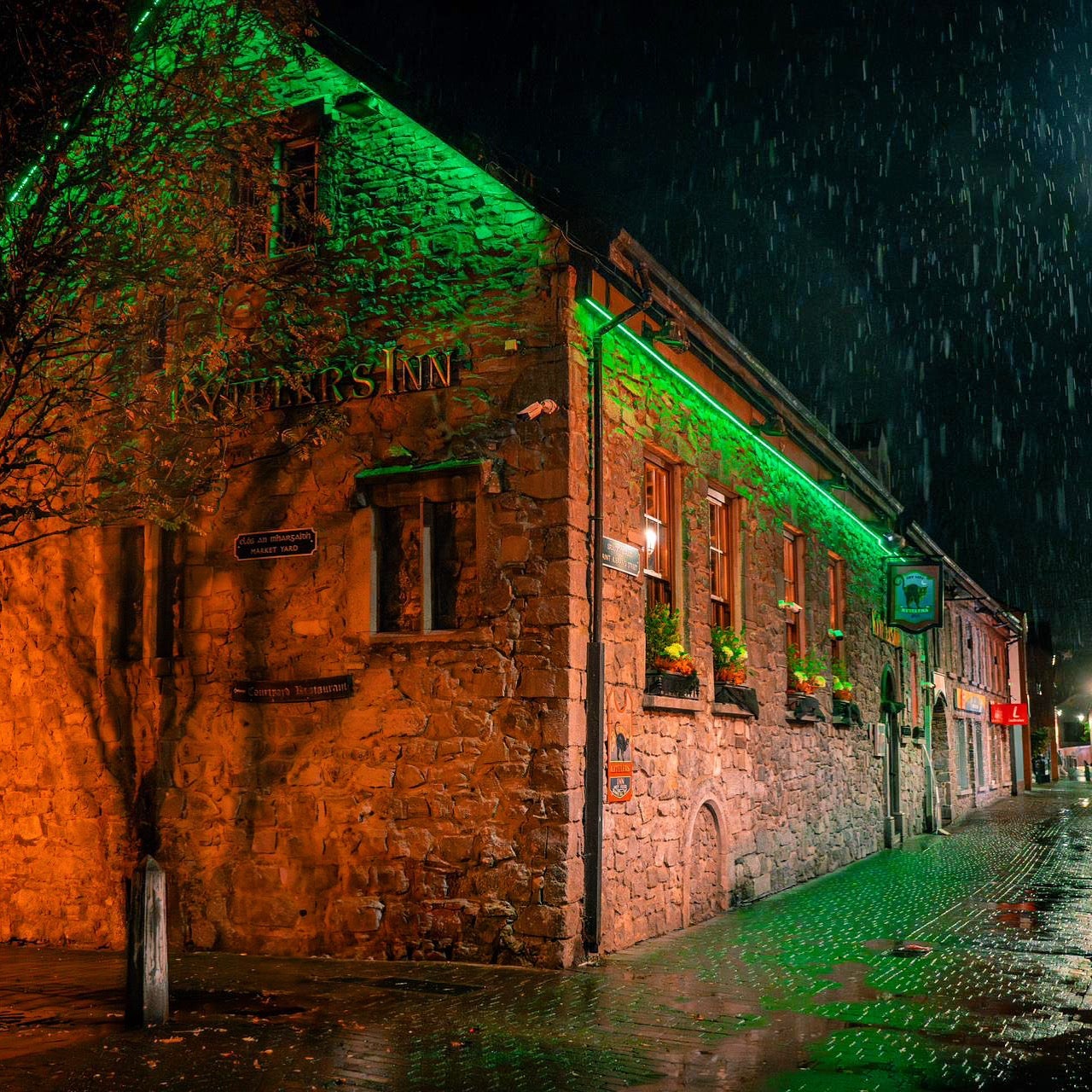Exterior of a stone pub with green lighting on a rainy night