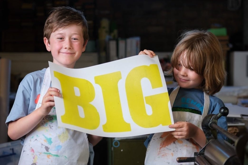 2 smiling young children holding up a large printed piece of paper with single large word on it.