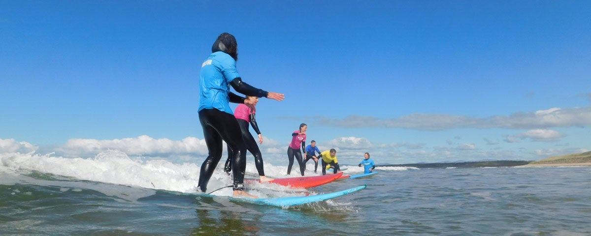 Kids on surf boards taking surfing lessons with an instructor in shallow waters