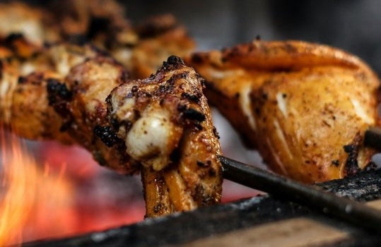 Close up view of meat on skewers cooking over flames.