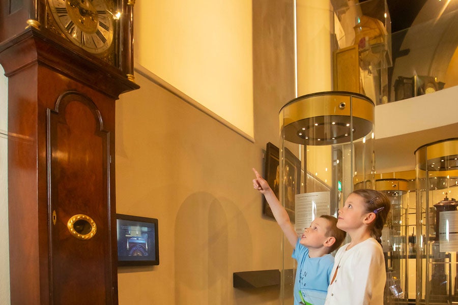 Two children looking up at a grandfather clock with one child is pointing up at it