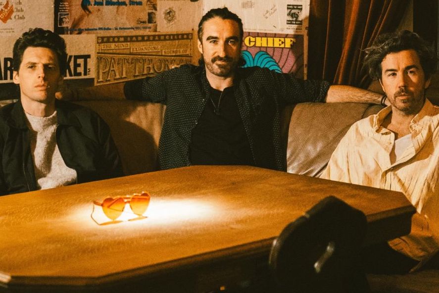 3 men seated around a wooden table on a corner couch