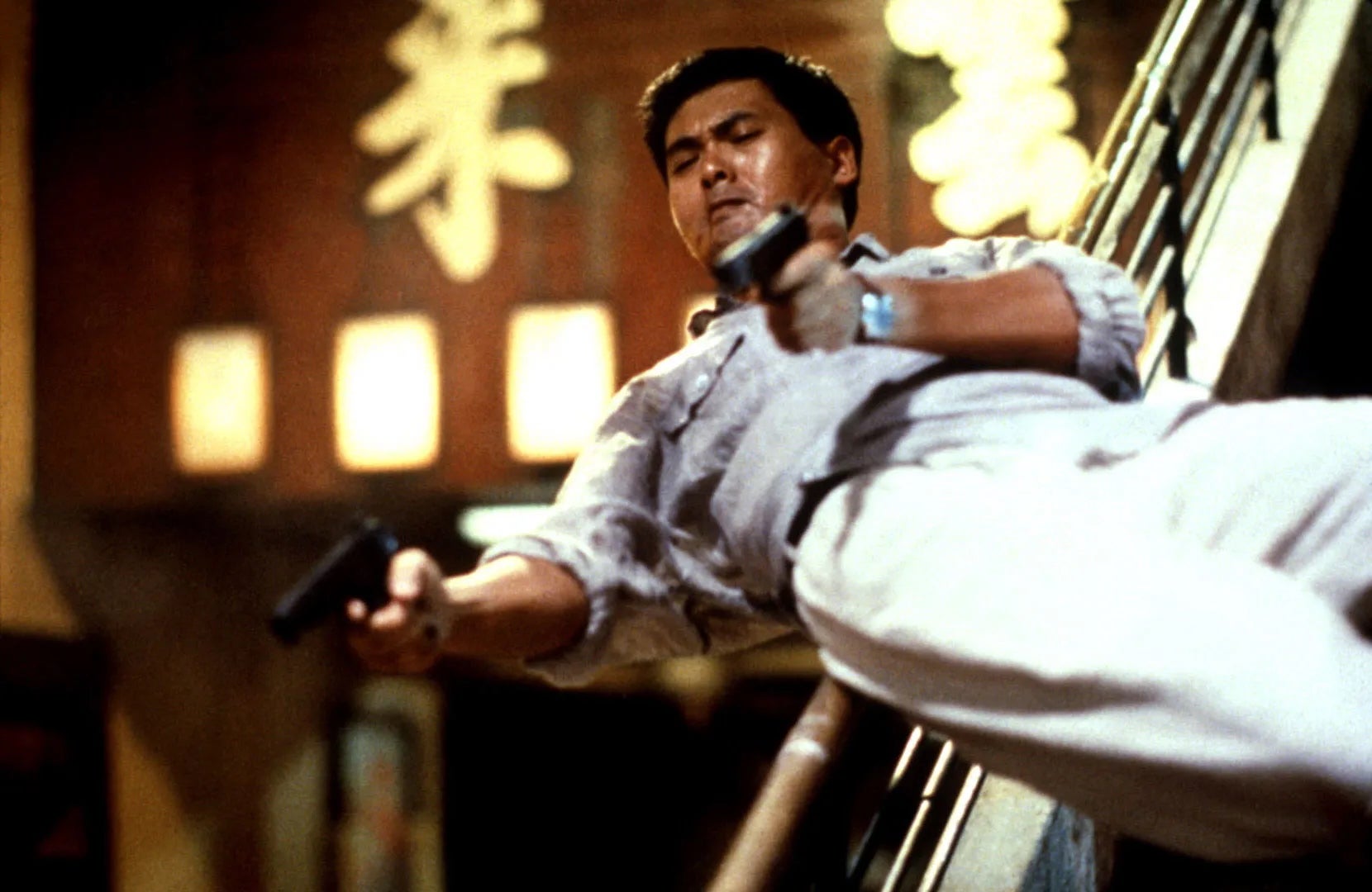 A man sliding down a banister, with a pistol in each hand.