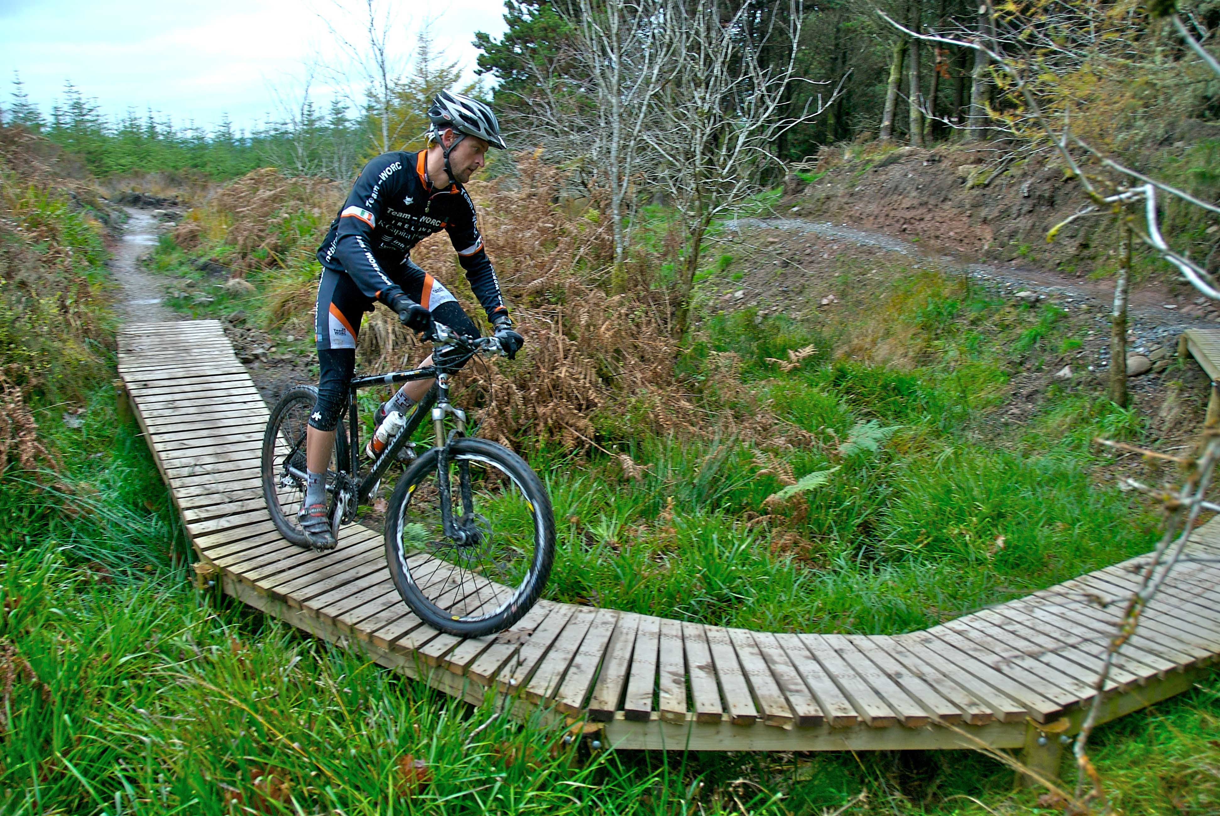 A man wearing biking gear and a helmet cycling on a boardwalk