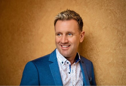 Mike Denver - a smiling man looking away to his right against dark gold background.
