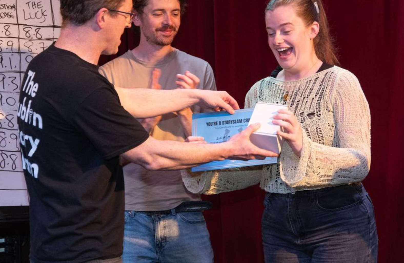 A man presenting a small box and certificate to a surprised looking woman.