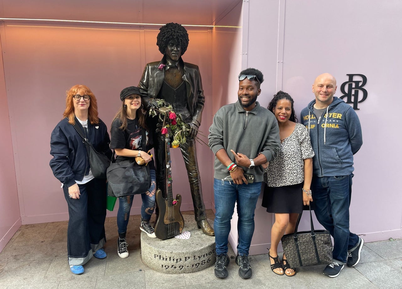 A walking group pose alongside a statue of the musician Phil Lynott