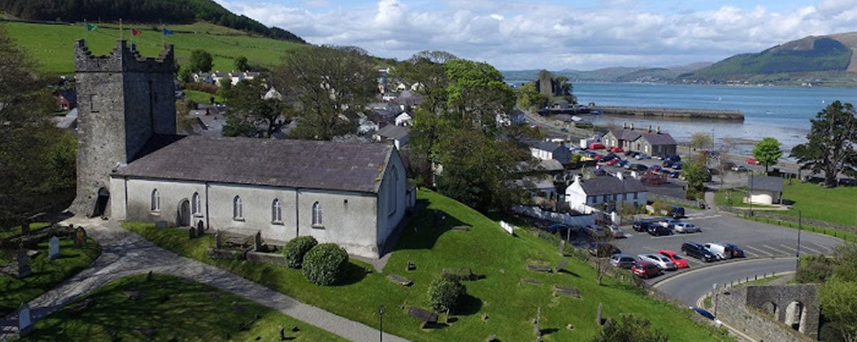 An old church on a small hill overlooking a town with the sea in the distance