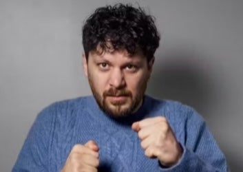 A man in blue knitted jumper holding his hands up in fists.