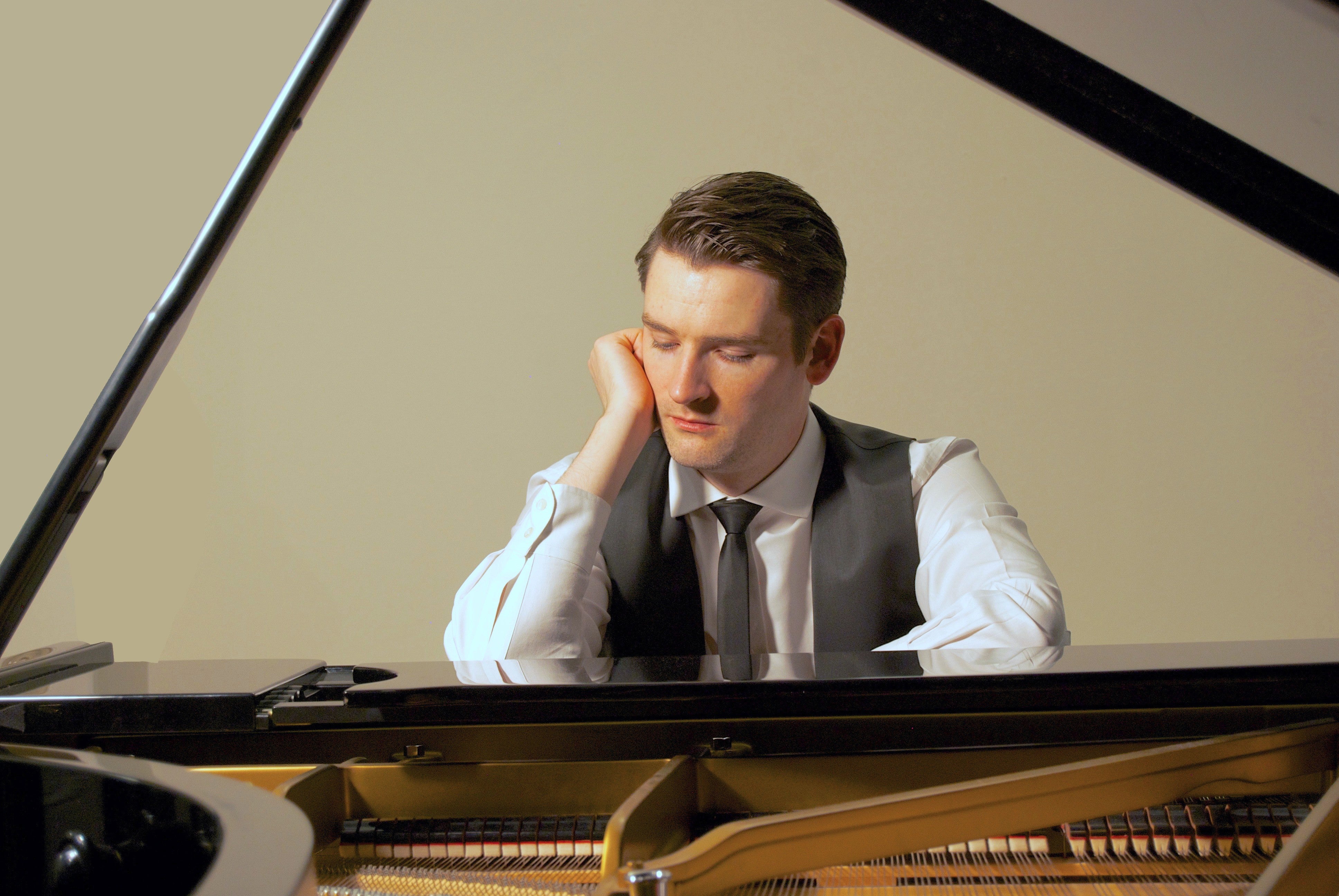 Michael McHale is resting his head on one of his hands as he sits pensively at a piano.