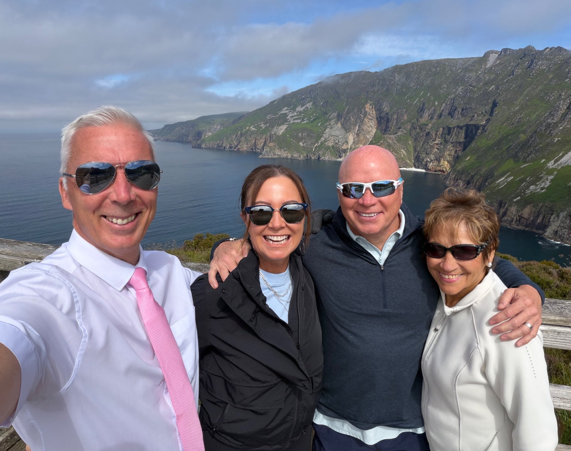 Four people wearing sunglasses pose for a selfie at the Cliffs of Moher