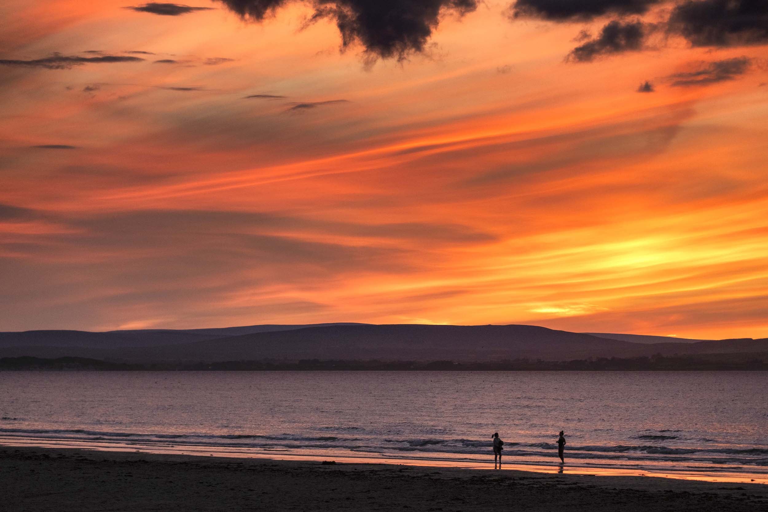 Two people walking on Enniscrone Beach in County Sligo at sunset.