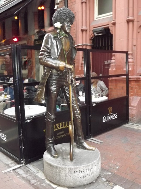 Bronze coloured statue of tall slim man holding a guitar upright in front of him