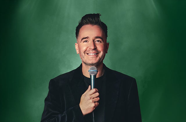 A smiling man holding up a mic to his chin.