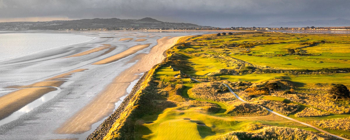 An aerial view of a golf course with sand dunes beside the sea