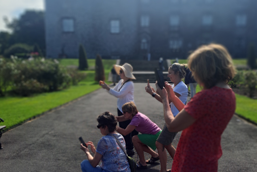 Kilkenny Leisure Phone Workshop, a group of people in gardens outside a castle, all pointing their phones in the same direction taking a photo.