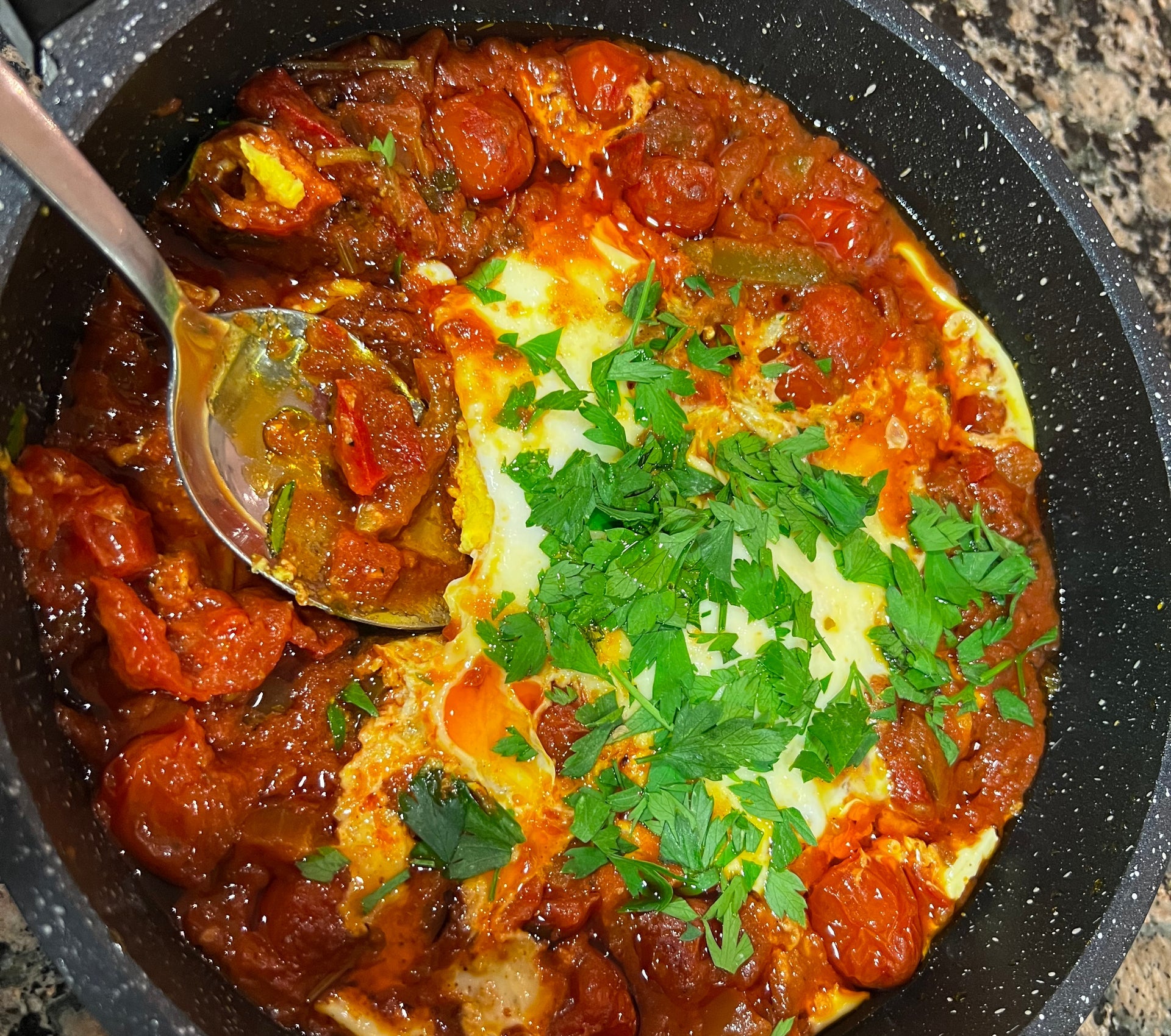 A pot with tomatoes and pasta mixed with a sauce sprinkled with green leaves