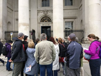 A group of people and a tour guide standing outside a stately building on a city street