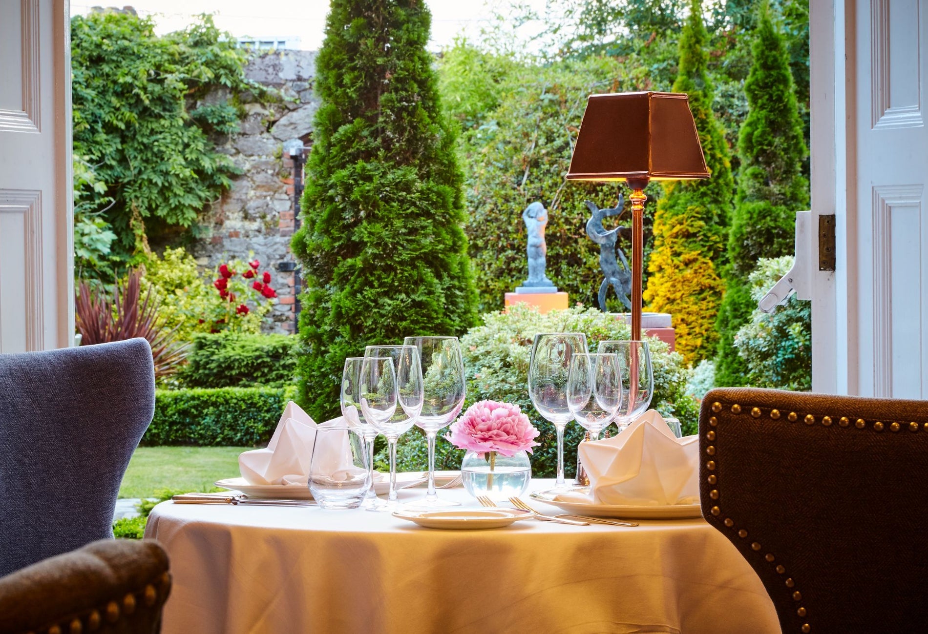 A set table with wine glasses next to a window overlooking a garden