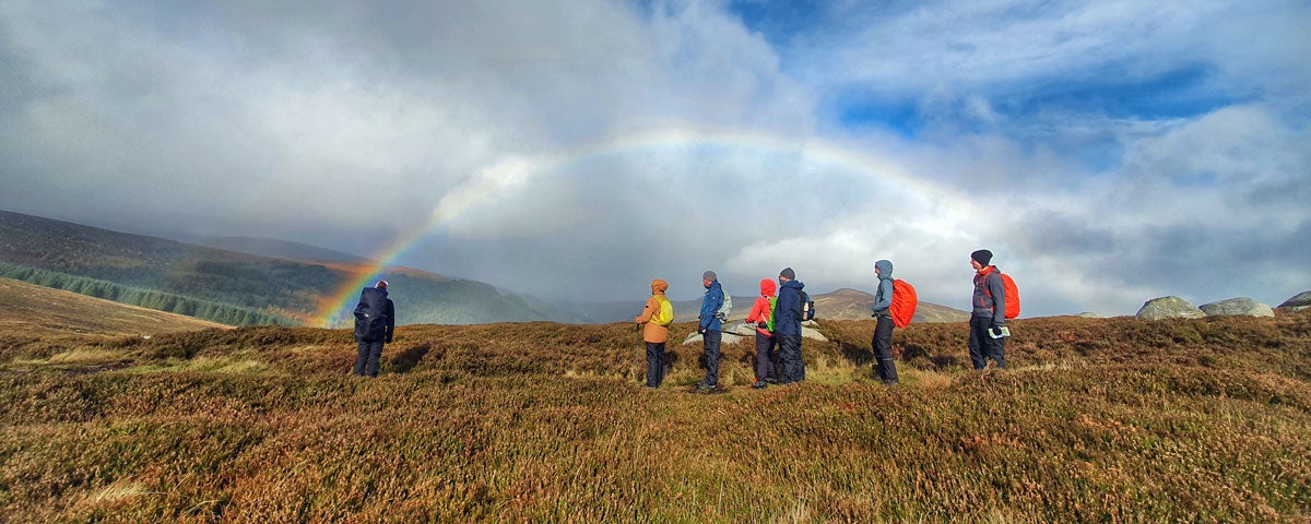 A group of walkers with the arc of a rainbow captured behind them in the distance