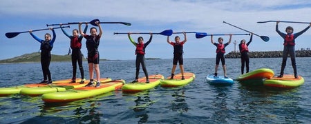 Eight children standing on paddleboards with their paddles held high over their heads