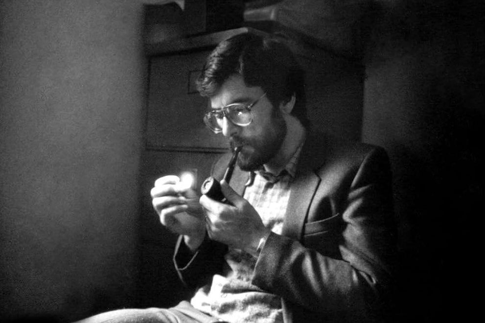 Black and white image of a seated man lighting a pipe.