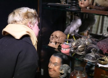 Visitor looking at a cabinet of curiosities including masks and false teeth