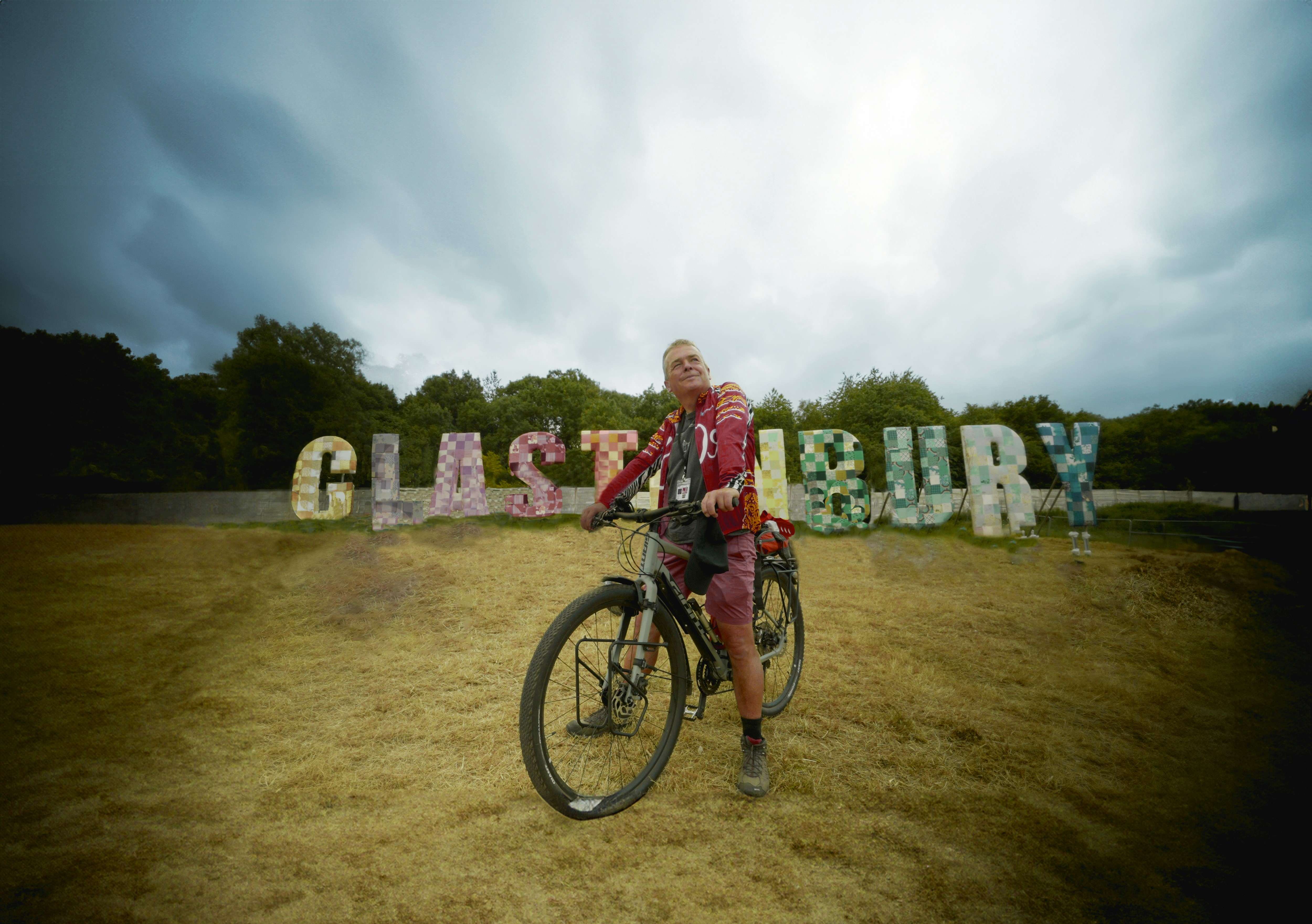 A man on a bicycle in front of letters that spell "Glastonbury".