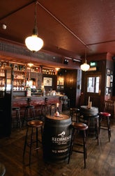 Interior of a traditional pub and bar with traditional dark wood tones and two wood barrels with stools as seating