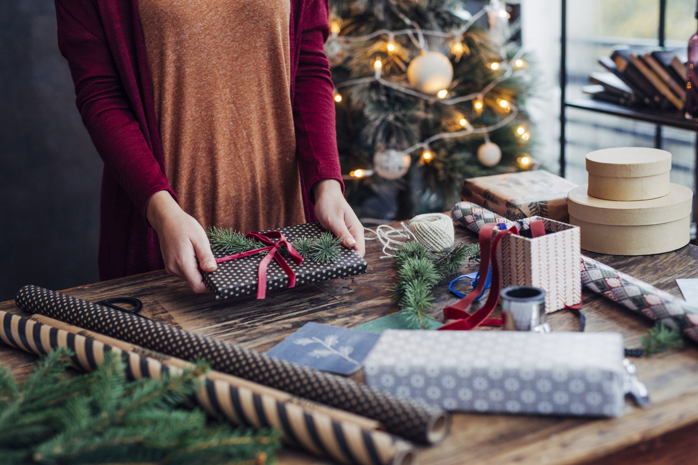 A person wrapping a present surrounded by wrapping paper and decorations