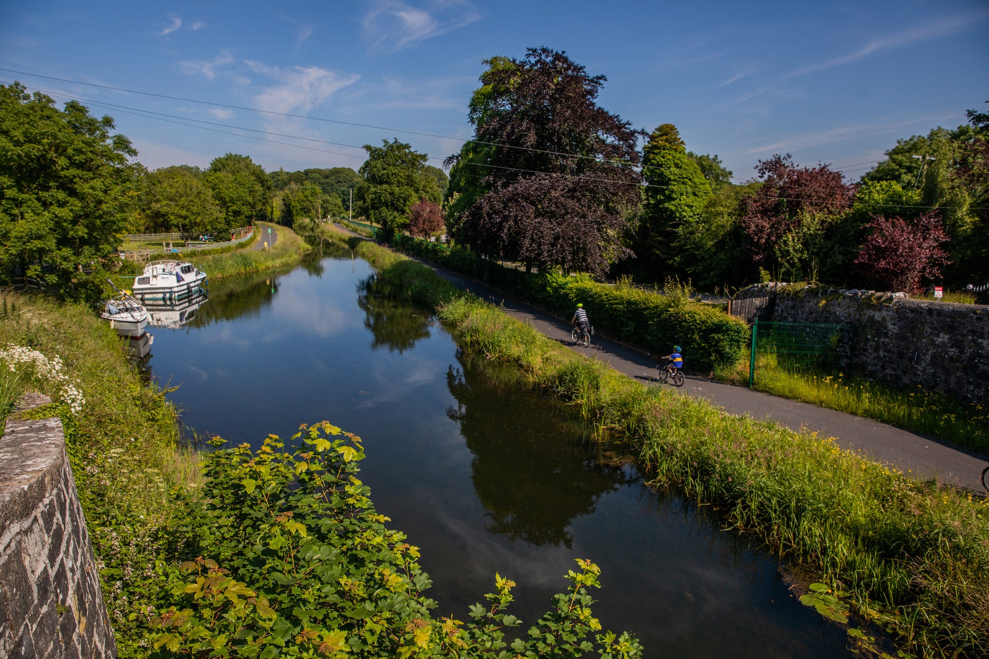Two people cycling past canal boats on the Royal Canal Greenway in County Westmeath.