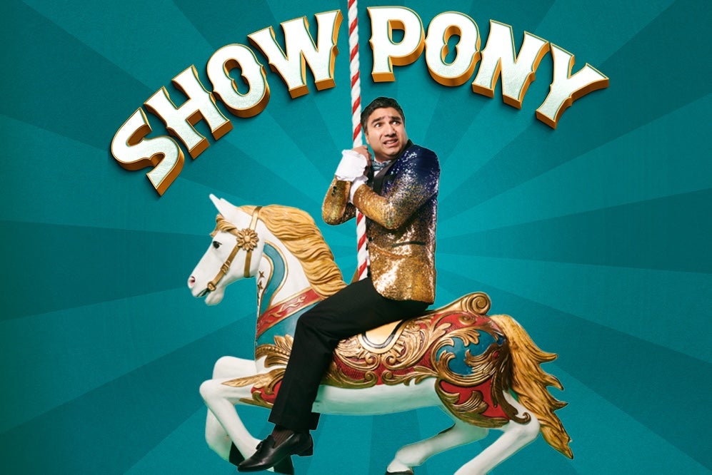 An anxious looking man in a gold sparkly jacket on the back of a decorated horse from a merry go round, clinging onto the stripy upright pole