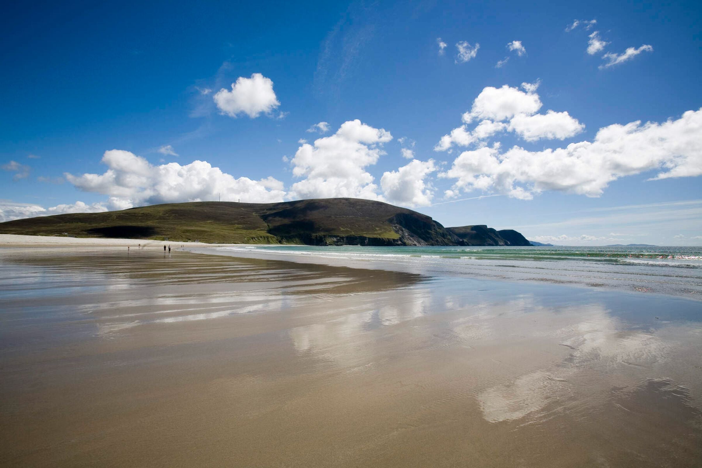 Keel Beach, Achill Island with blue sky, fluffy clouds, and reflections on wet sand