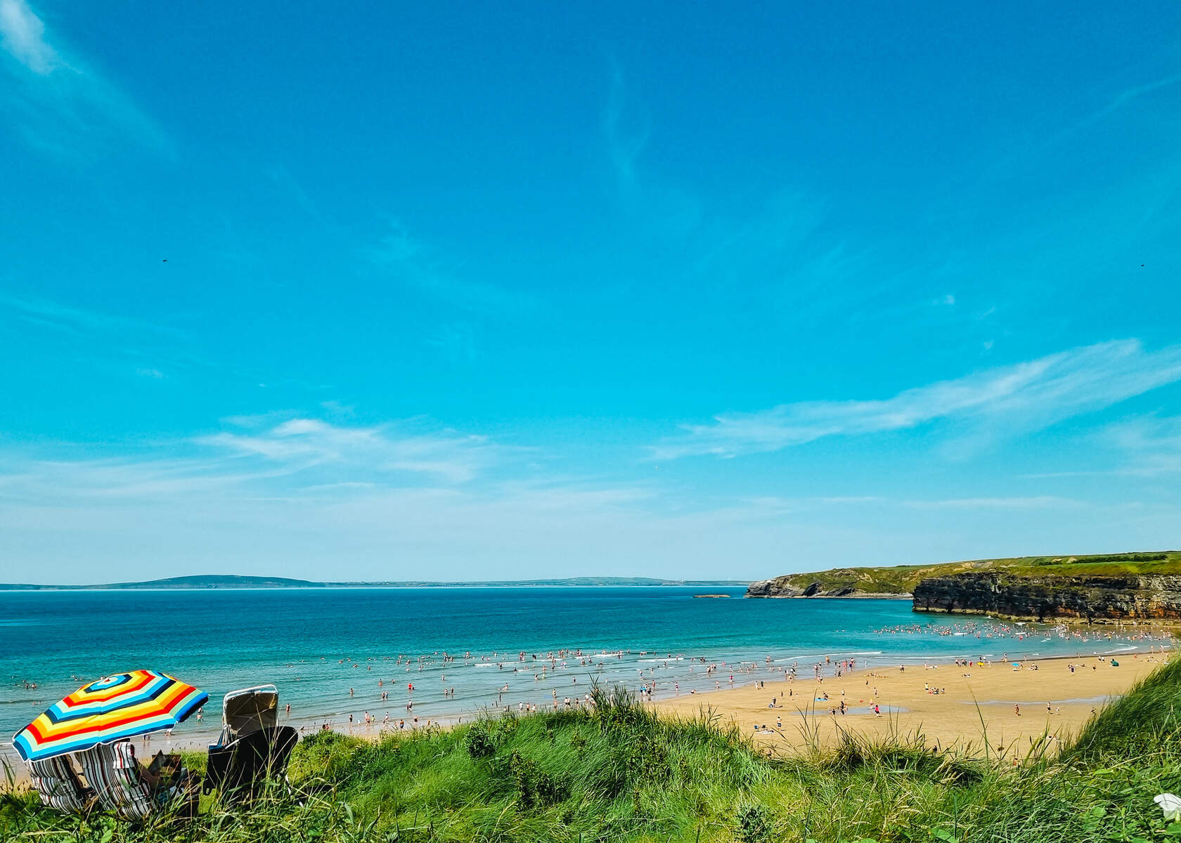 Colourful umbrella and chairs above a beach with cliffs, sea and blue sky