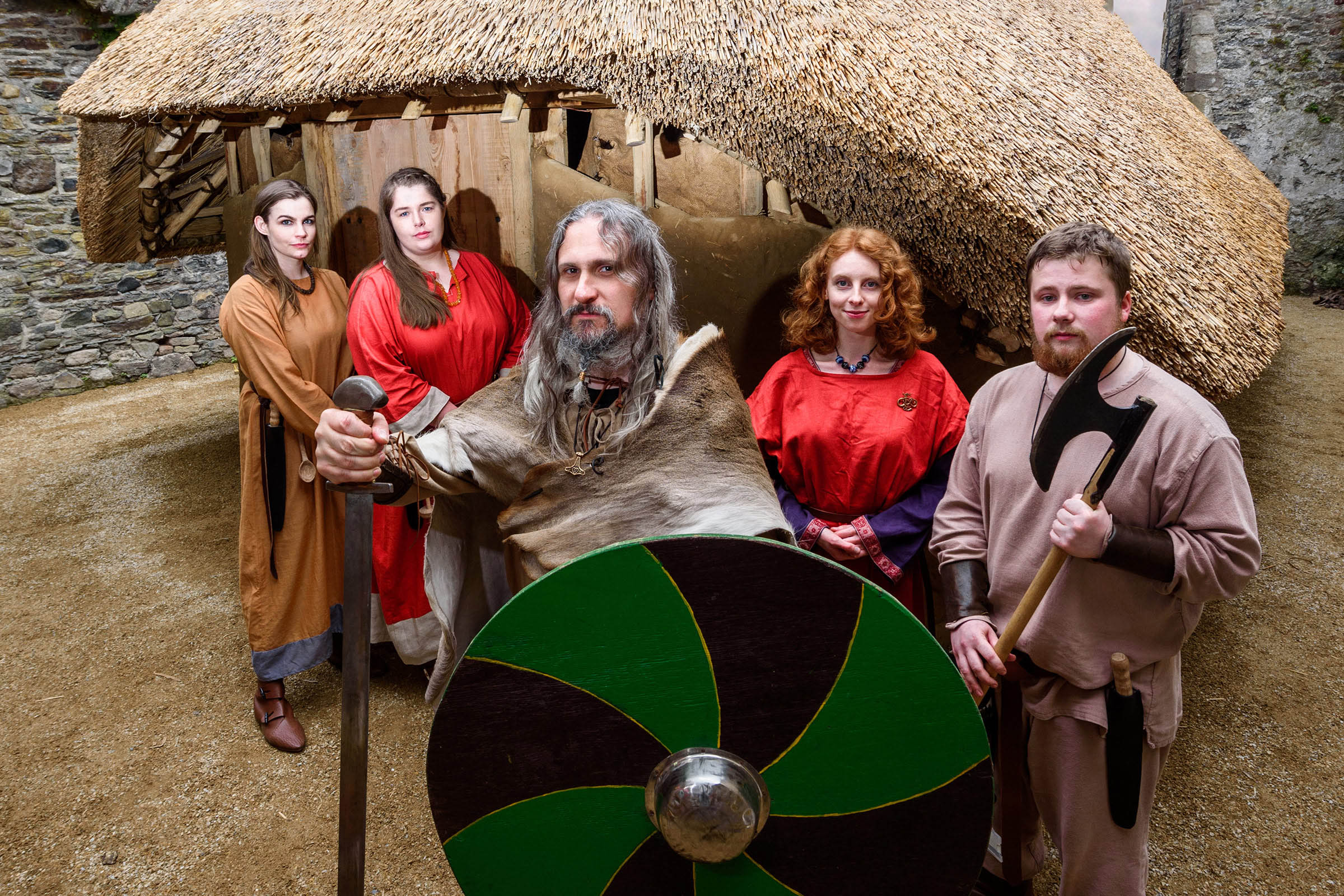 A group of Viking reenactors stand in front of a building carrying a sword, shield and axe.
